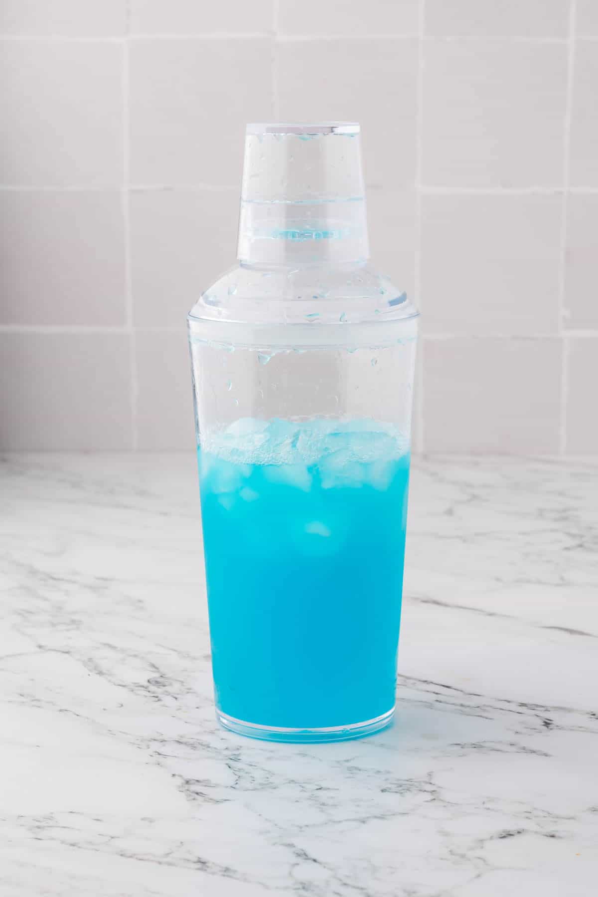 Combining ingredients for a blue lagoon mocktail in a clear shaker.