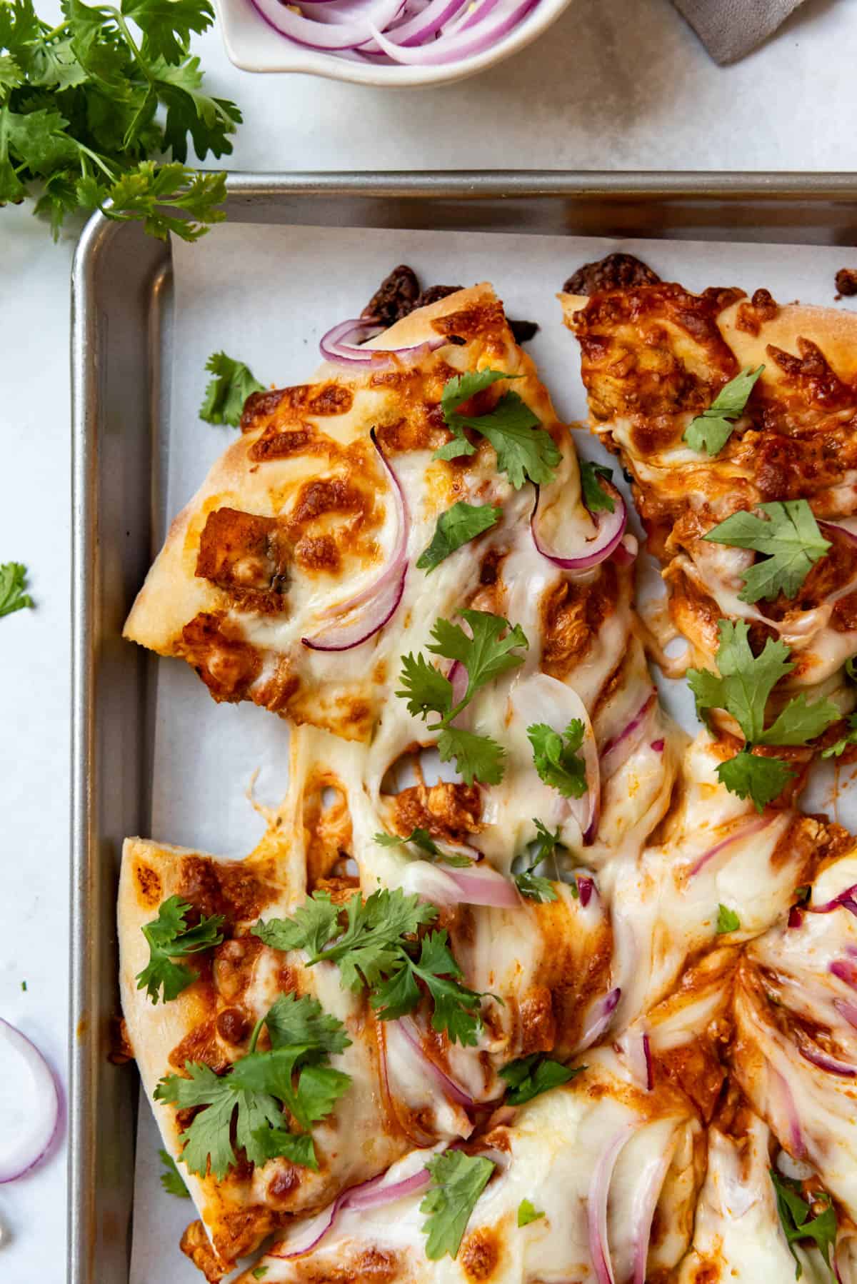 An overhead image of slices of chicken tikka masala pizza on a baking sheet lined with parchment paper.