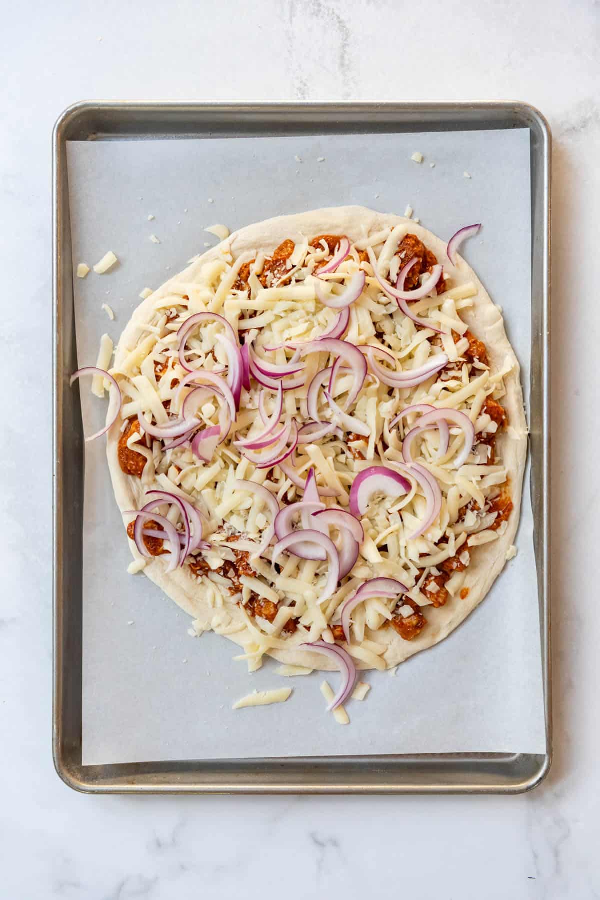 Adding shredded mozzarella cheese and thinly sliced red onions to a pizza before baking.