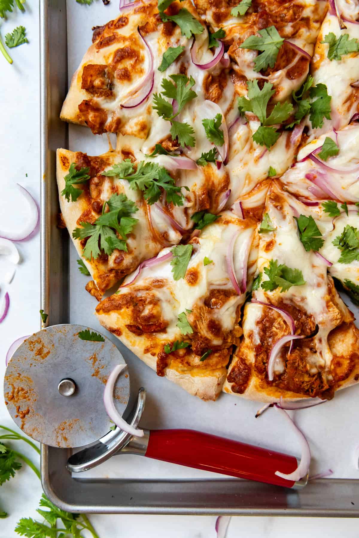 A close up image of a sliced pizza with chicken tikka masala sauce, fresh cilantro, and red onions on top.