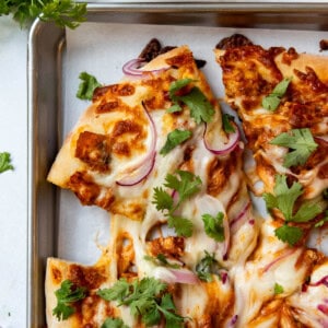 An overhead image of slices of chicken tikka masala pizza on a baking sheet lined with parchment paper.