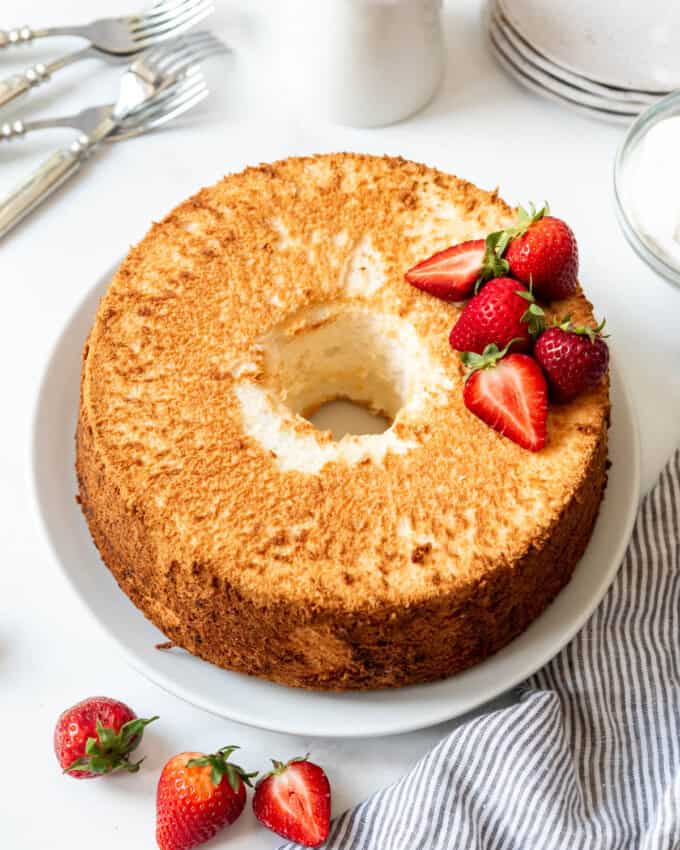 An overhead image of a light and fluffy angel food cake on a white plate decorated with halved strawberries.