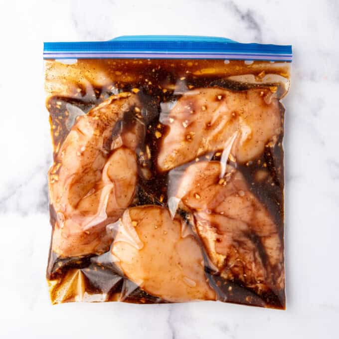 A ziploc bag full of chicken in a marinade on a white marble surface.