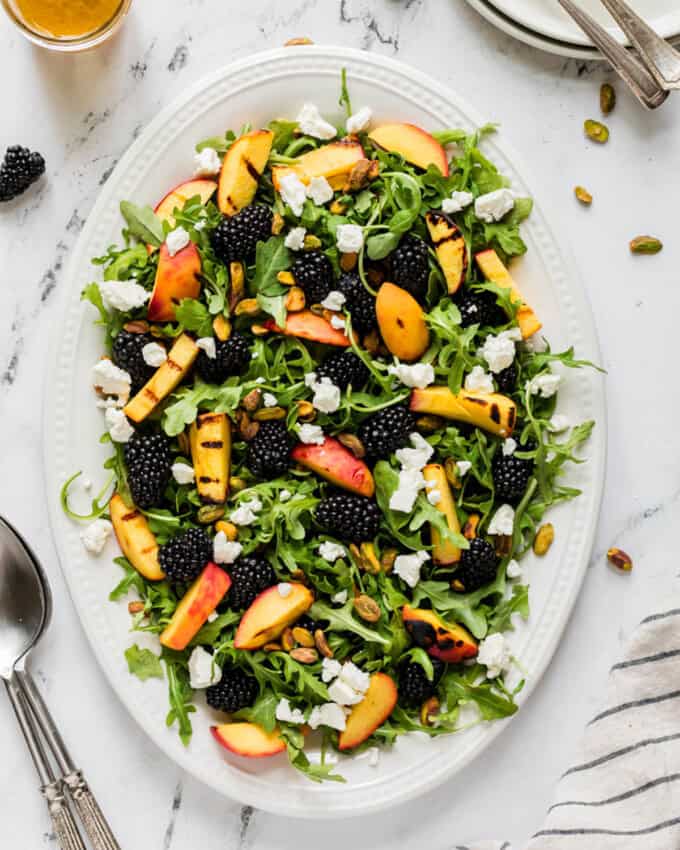 An overhead image of a large summer salad made with grilled peaches, blackberries, and arugula.