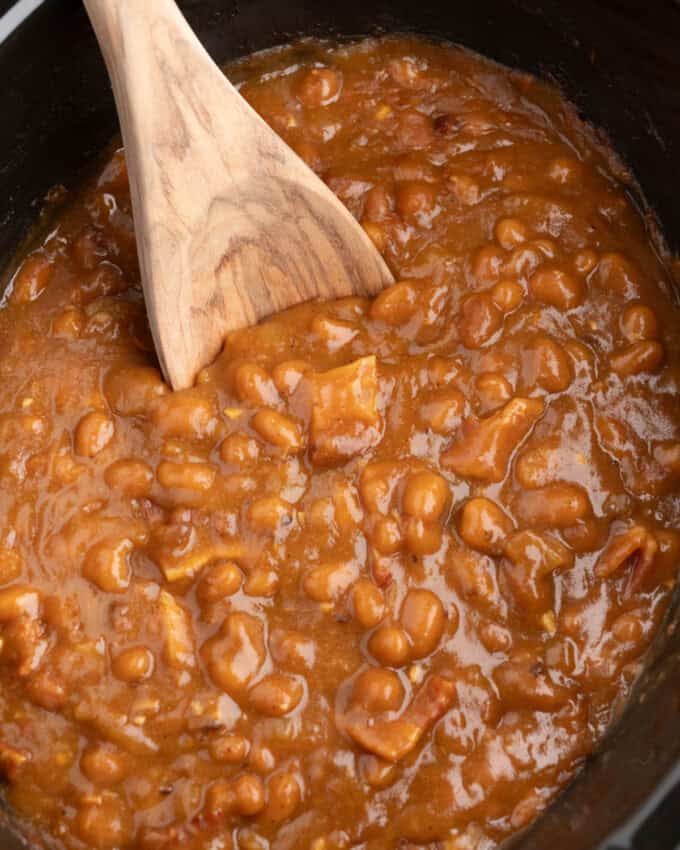 A close image of a wooden spoon in a batch of baked beans.