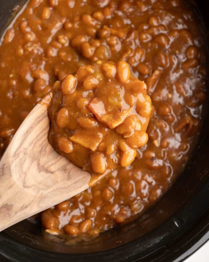 A wooden spoon lifting a scoop of baked beans.