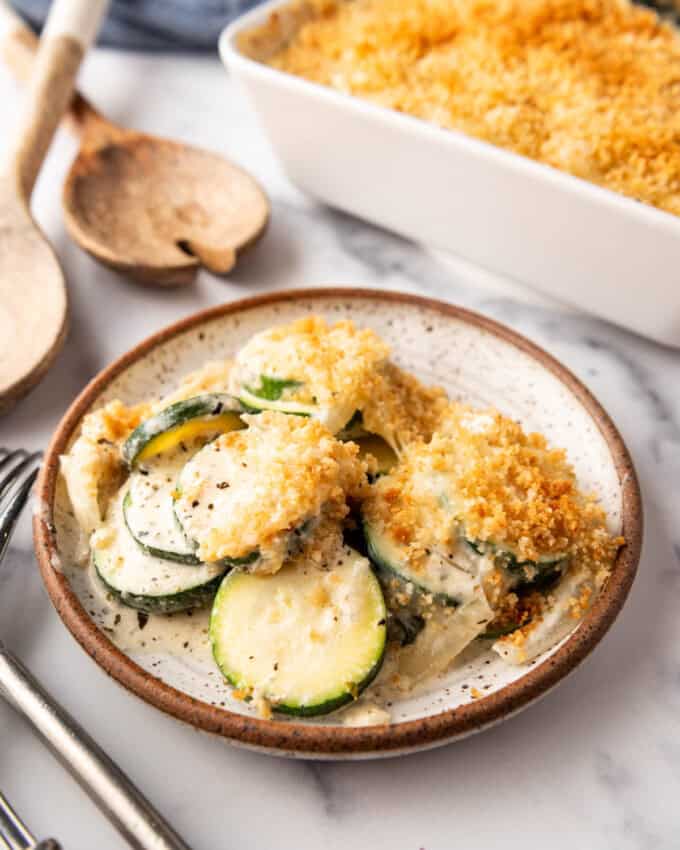 A plate of zucchini casserole in front of a white baking dish.