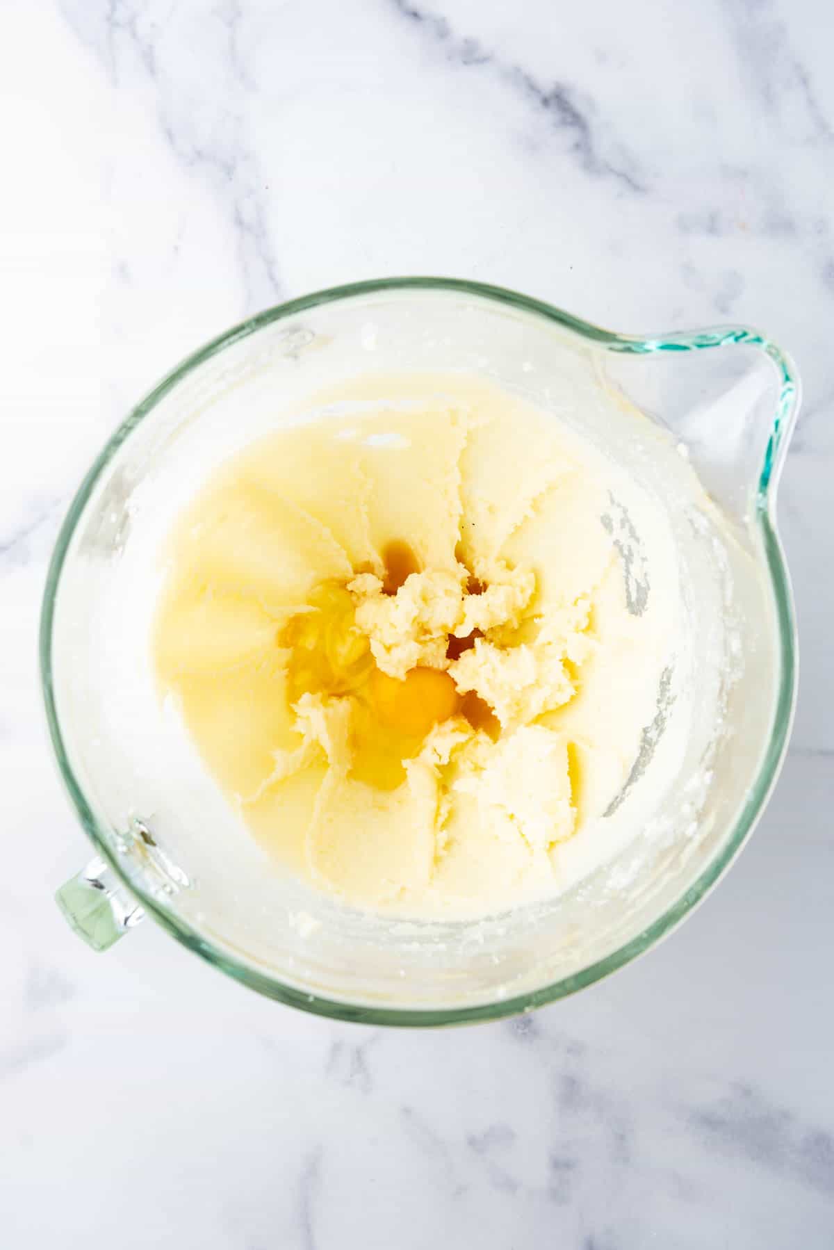 Adding an egg and vanilla extract to creamed butter and sugar in a glass mixing bowl.