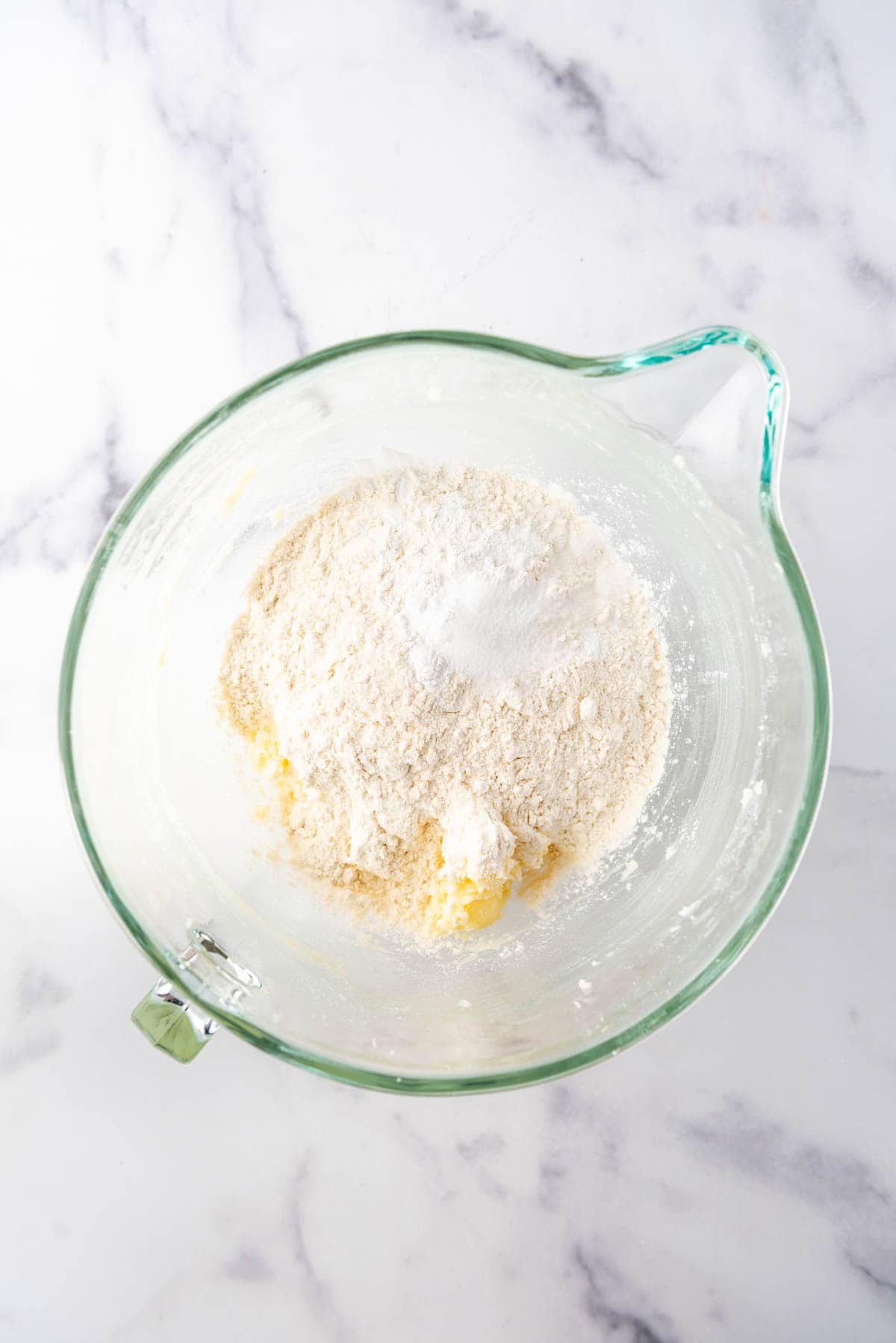 Adding dry ingredients to cookie dough in a large glass mixing bowl.