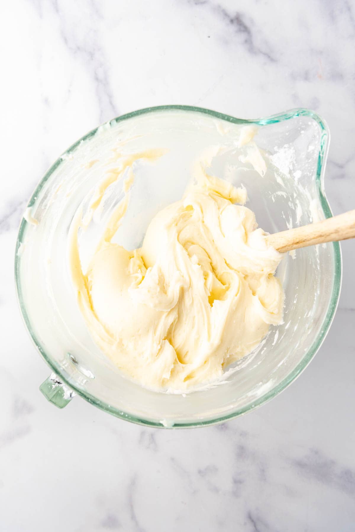 An overhead image of a bowl of cream cheese frosting with a spatula in it.