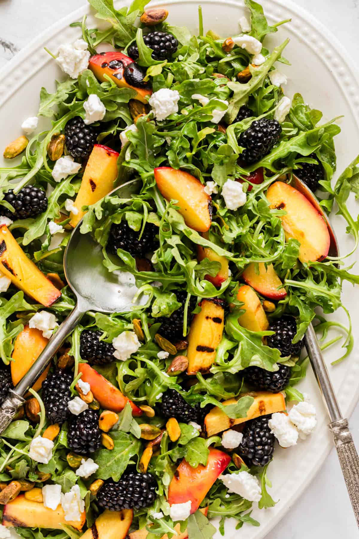 An overhead image of a grilled peach salad with serving spoons in it.