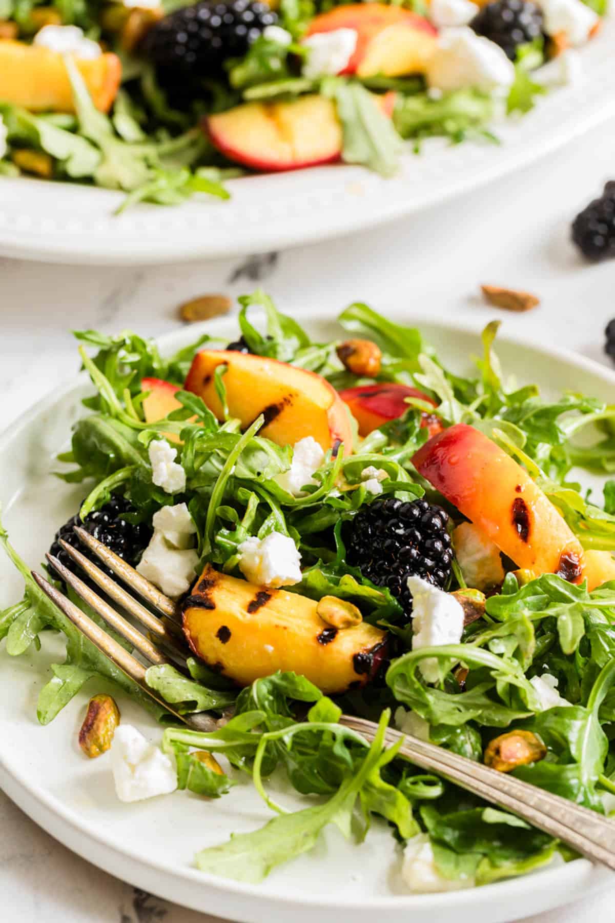 A plate of grilled peach salad with a fork on it.