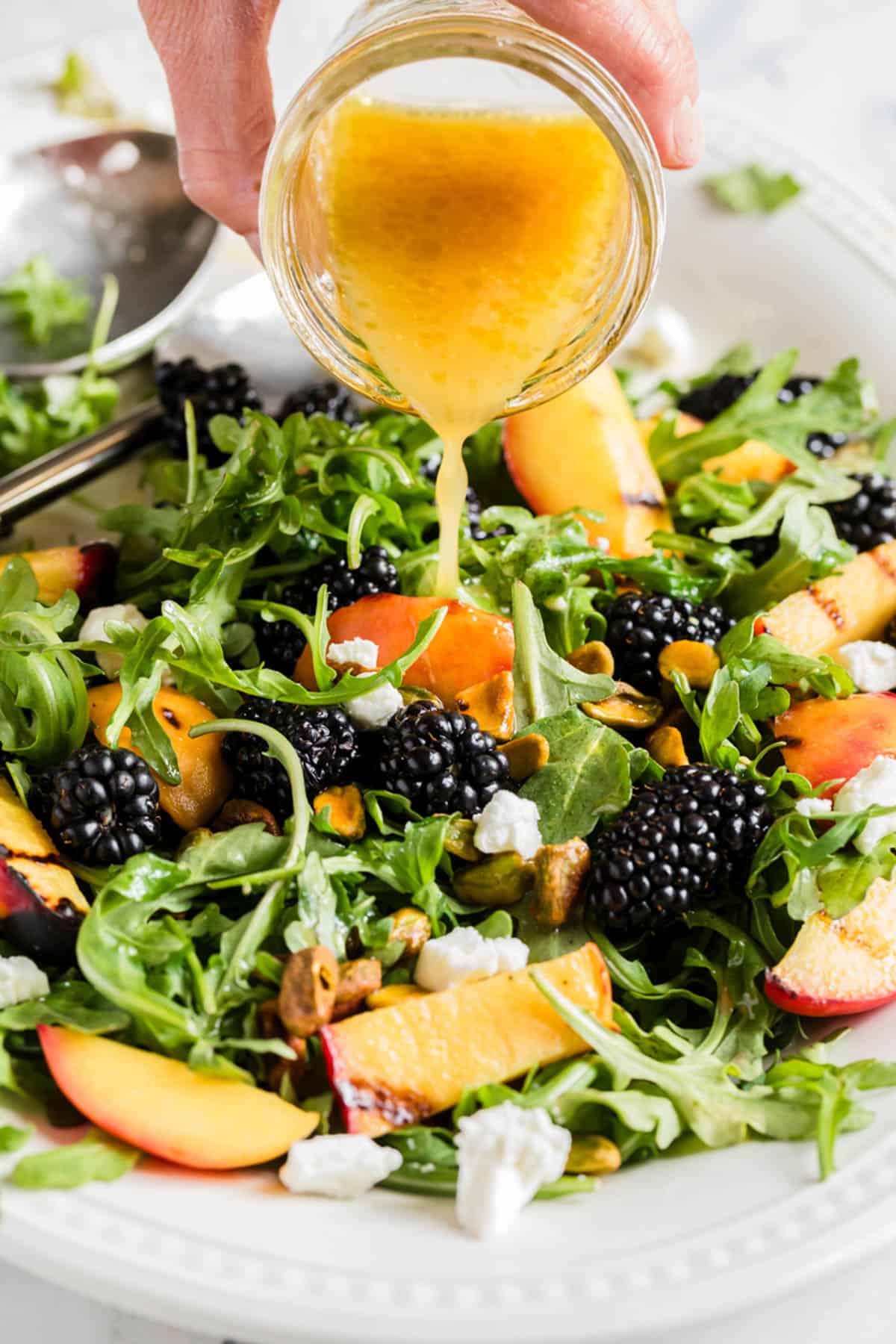 A hand pouring vinaigrette from a glass jar.