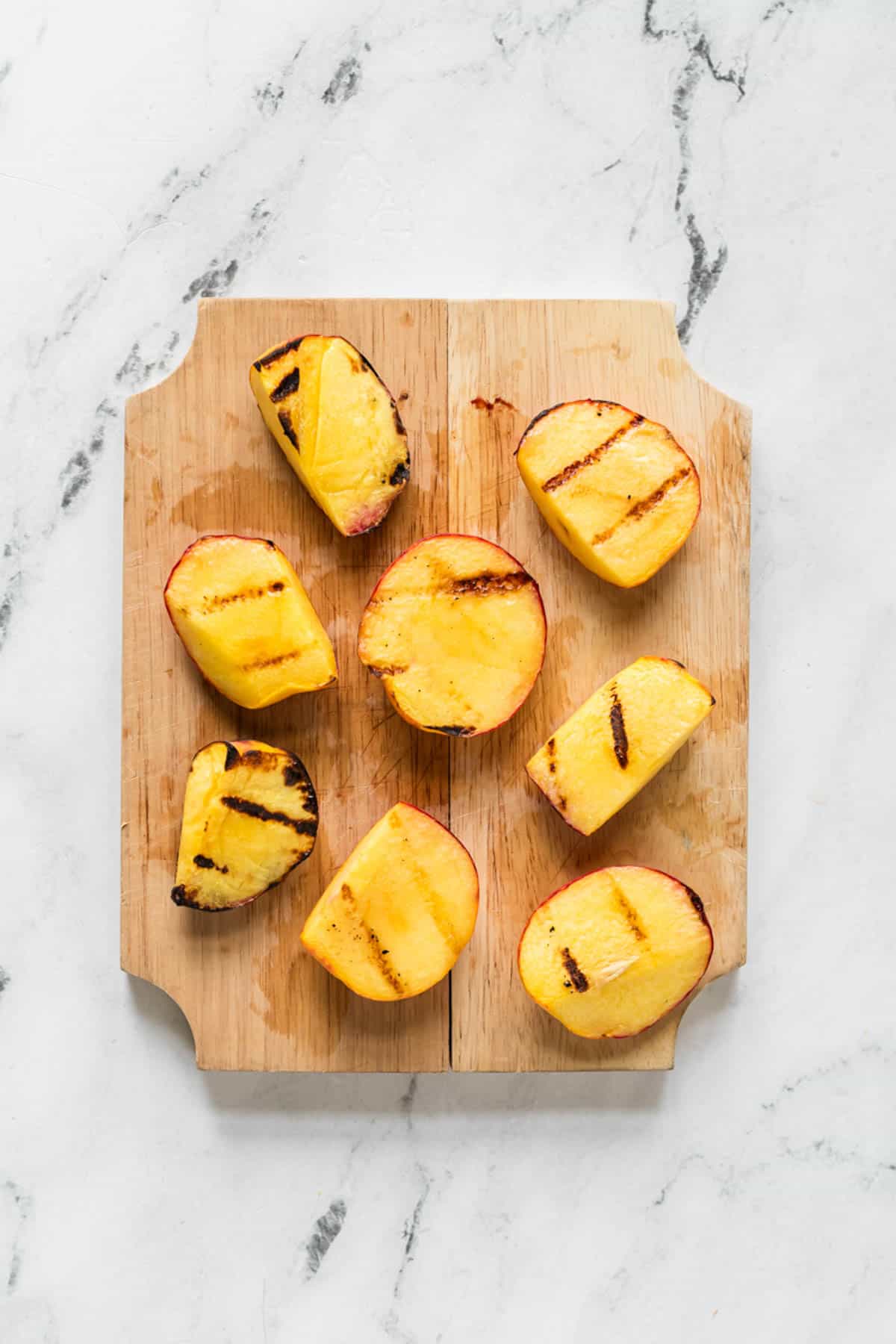 Grilled peaches on a cutting board.