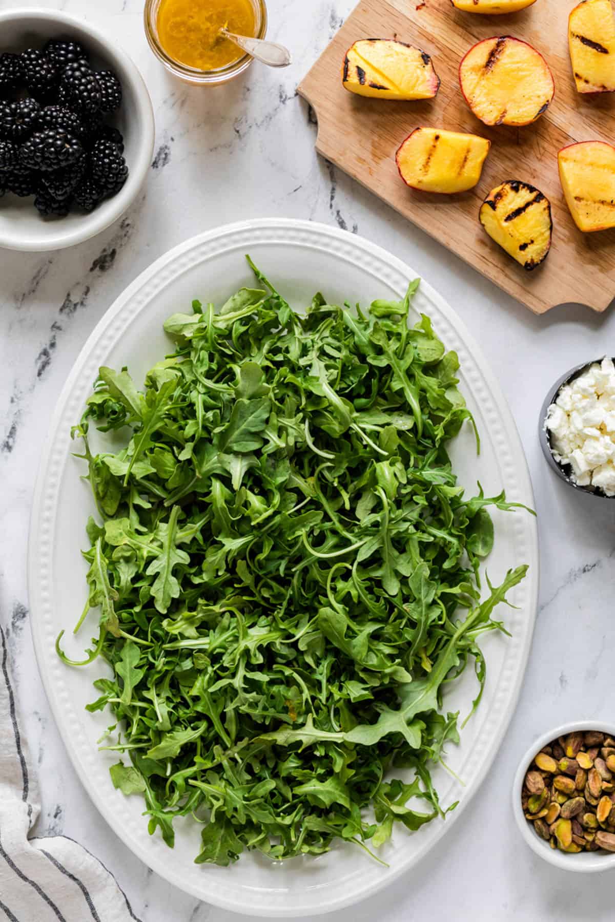 A large white plate of arugula surrounded by other salad ingredients.