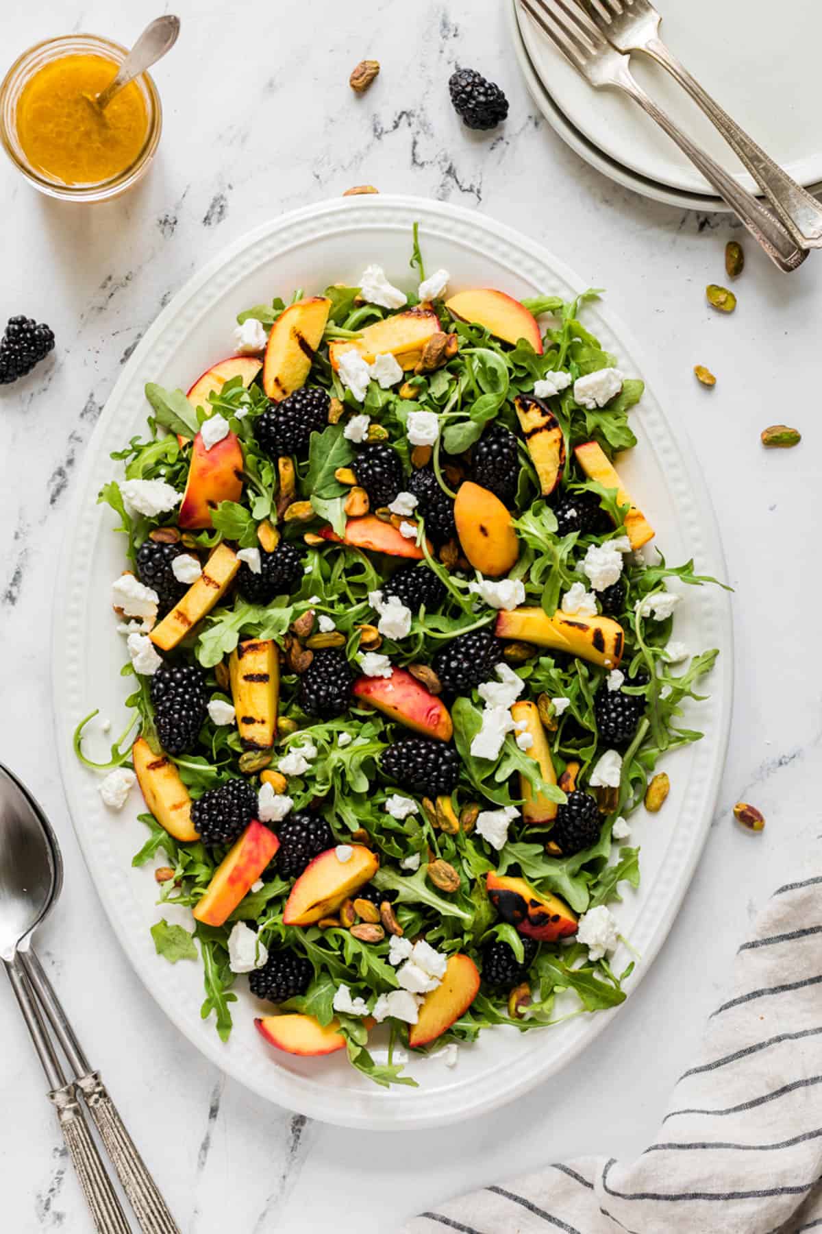 An overhead image of a large summer salad made with grilled peaches, blackberries, and arugula.