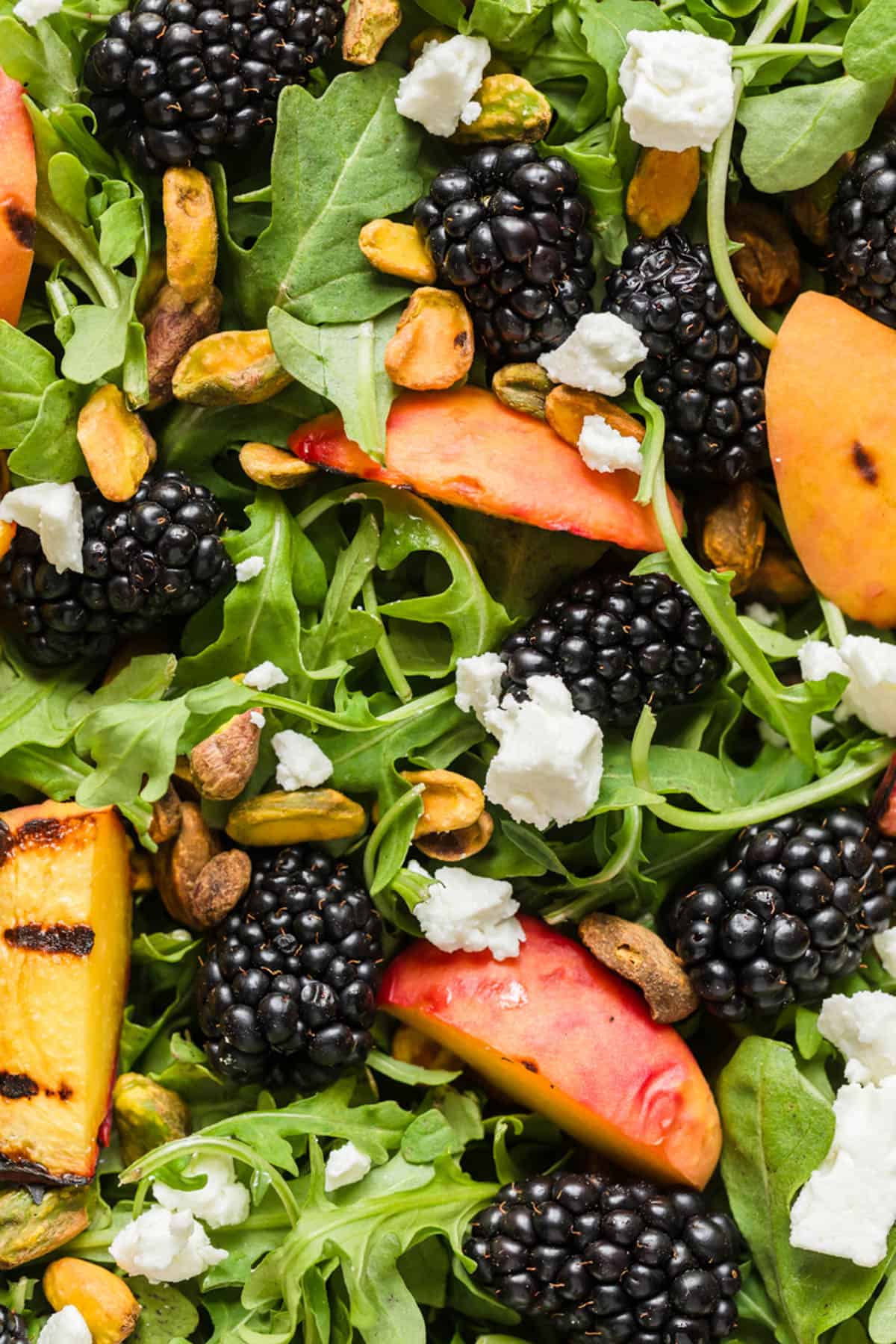 A close up image of blackberries, grilled peaches, feta cheese, and arugula.