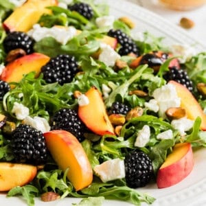 A close image of grilled peach salad with arugula and blackberries.