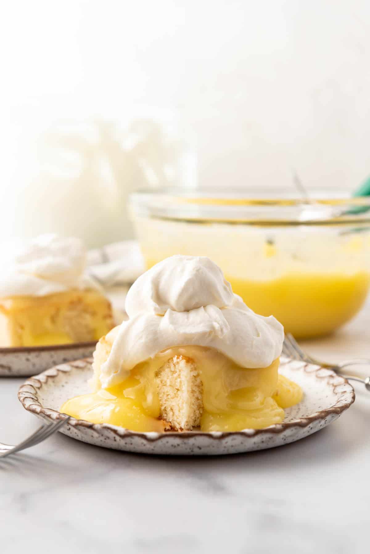 A slice of white cake with homemade lemon pudding and whipped cream on top.