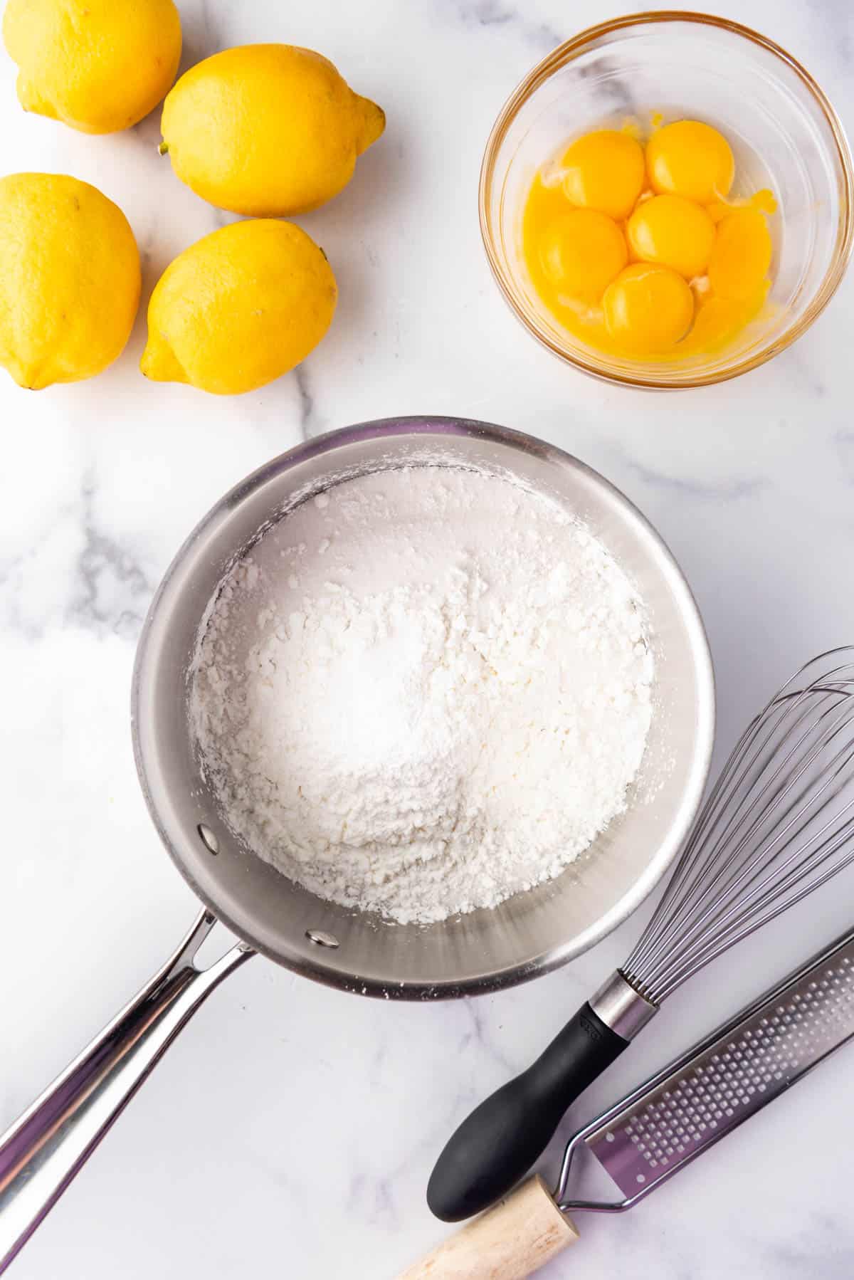 Cornstarch and granulated sugar in a medium saucepan next to egg yolks and lemons.