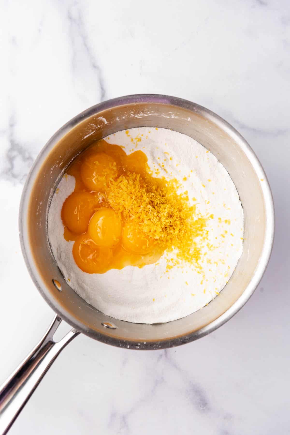 Adding egg yolks and lemon zest to granulated sugar and cornstarch in a medium saucepan.