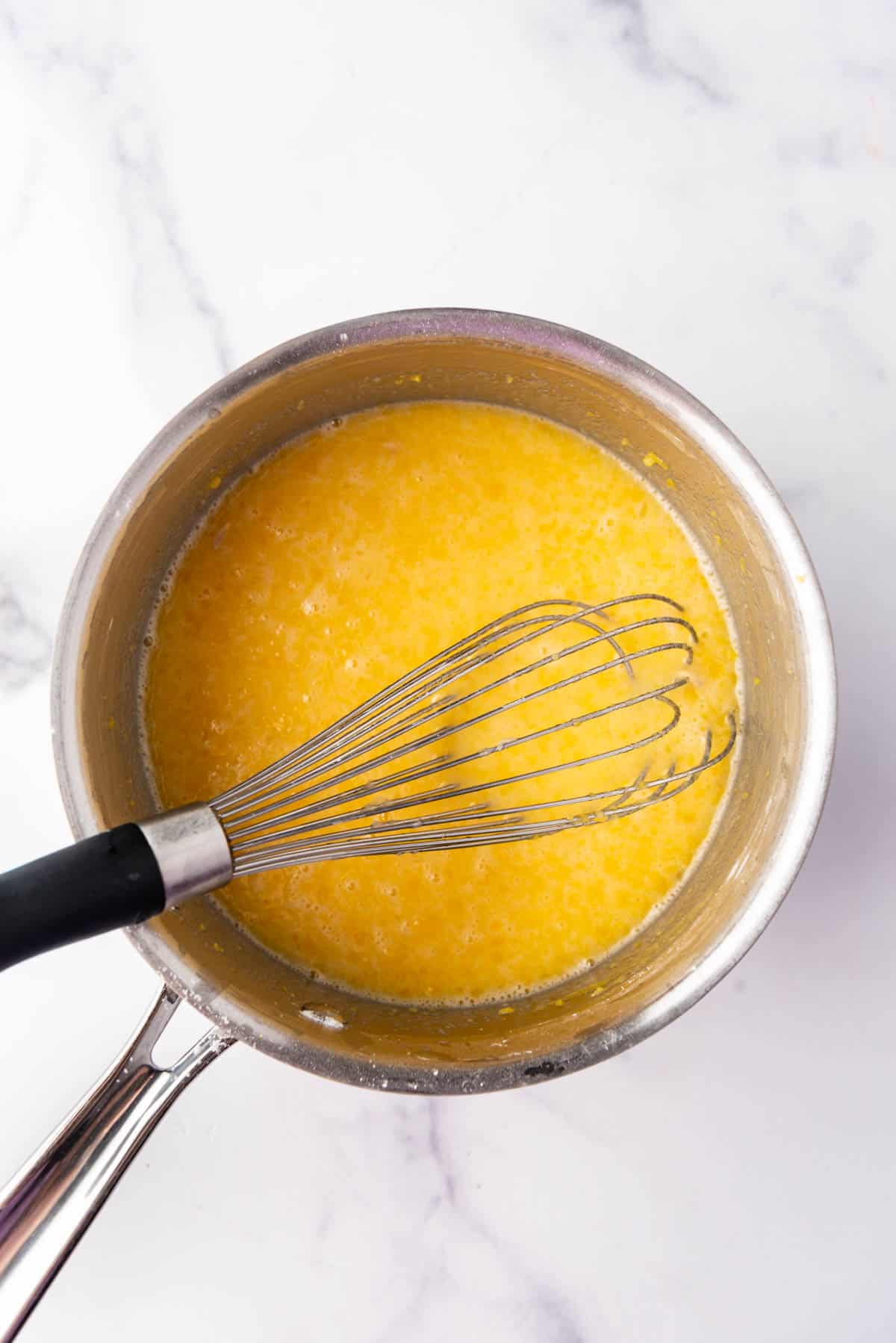 A whisk in a saucepan full of lemon pudding ingredients.