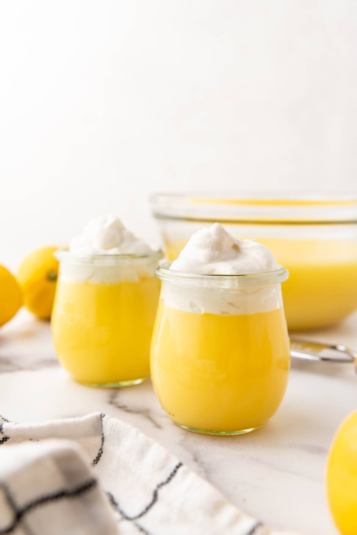 Two cups of lemon pudding in front of a large glass bowl of more lemon pudding.