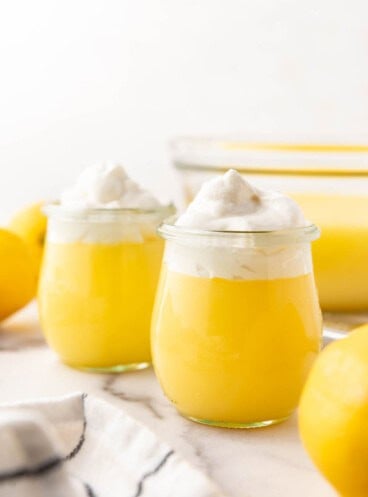 An image of two glass cups of lemon pudding with whipped cream on top.