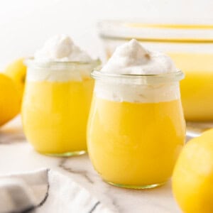 An image of two glass cups of lemon pudding with whipped cream on top.