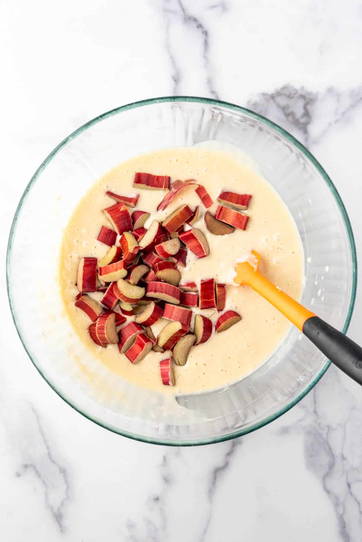 Adding chopped rhubarb to quick bread batter in a mixing bowl with a spatula.