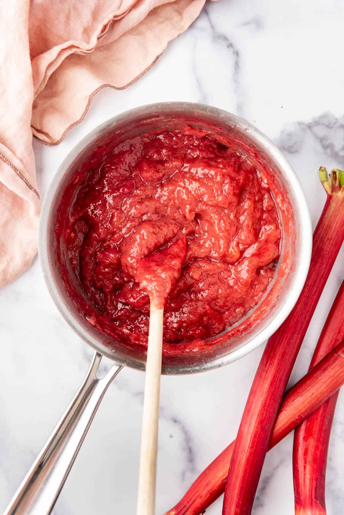 An overhead image of a pot of rhubarb sauce next to rhubarb stalks.