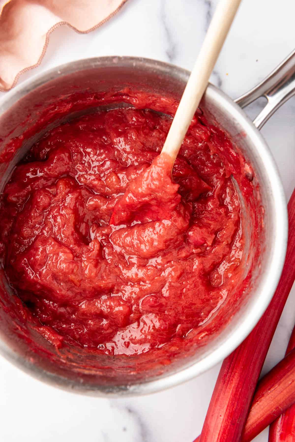 An overhead image of rhubarb sauce in a pot with a wooden spoon.