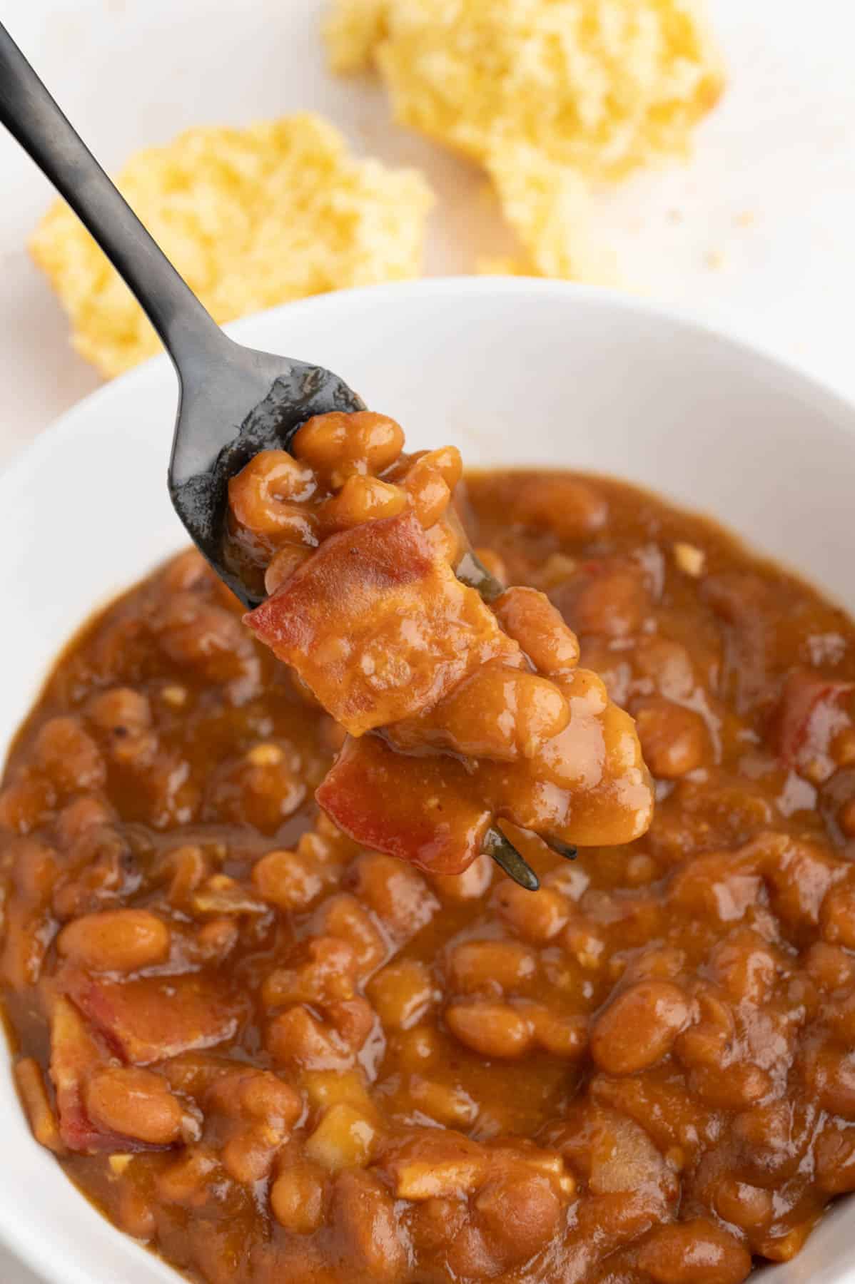 A fork lifting a mouthful of baked beans with bacon.