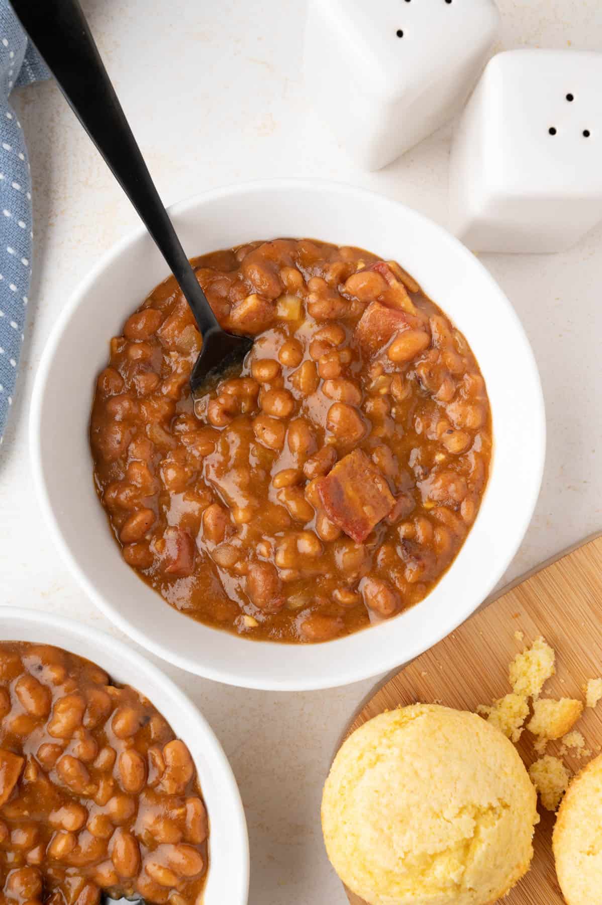 An overhead image of a bowl of baked beans next to corn muffins.