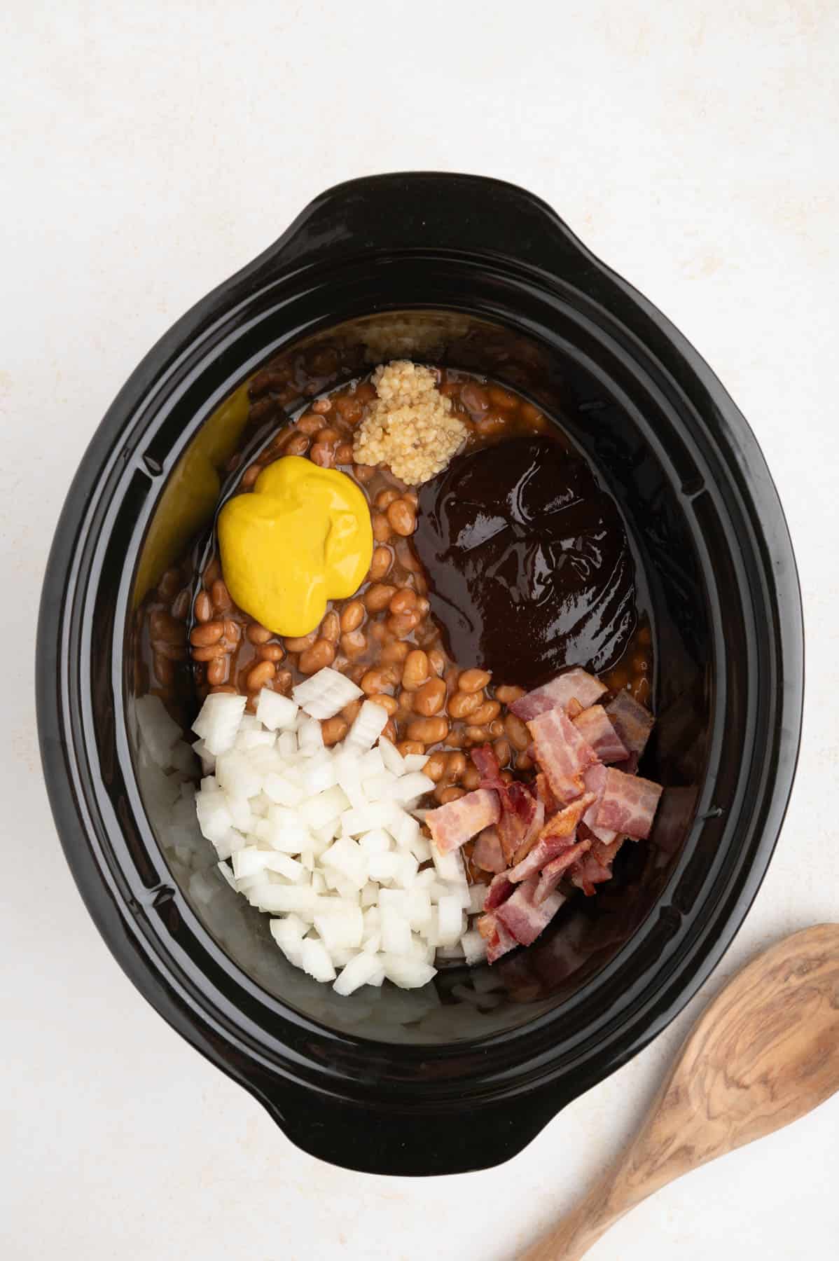 Ingredients for slow cooker baked beans in a crockpot before stirring them together.