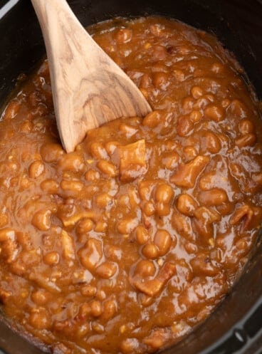 A close image of a wooden spoon in a batch of baked beans.