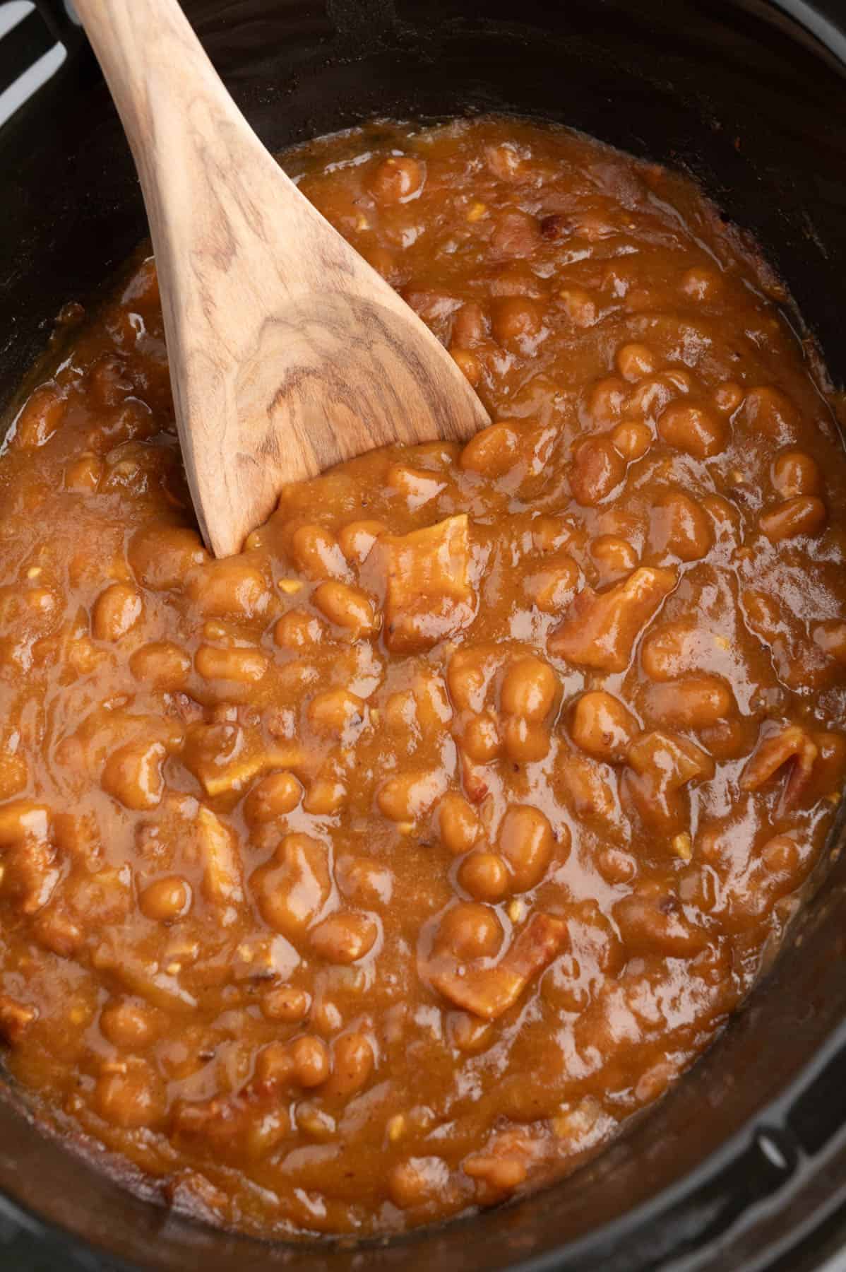 A close image of a wooden spoon in a batch of baked beans.