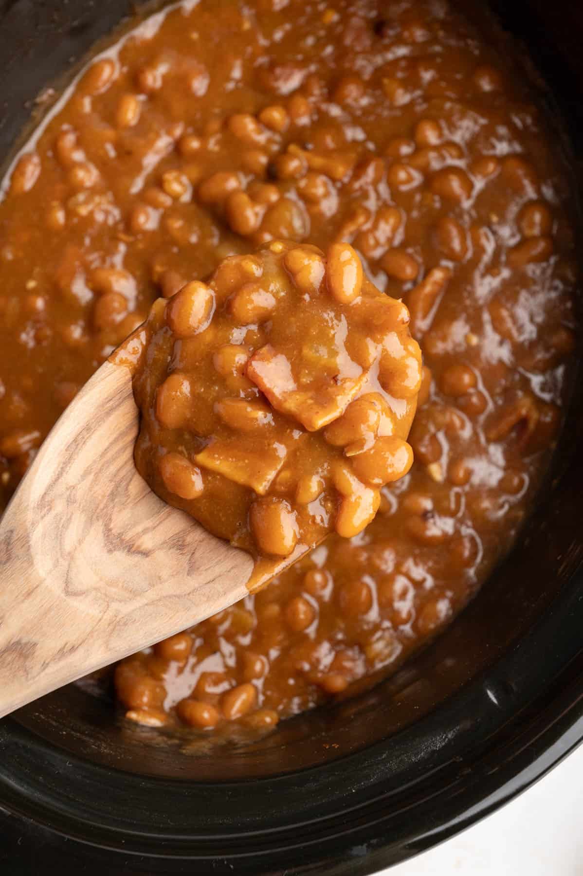 A wooden spoon lifting a scoop of baked beans.