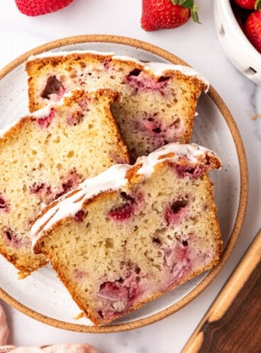 An overhead image of slices of moist strawberry quick bread on a plate surrounded by strawberries.