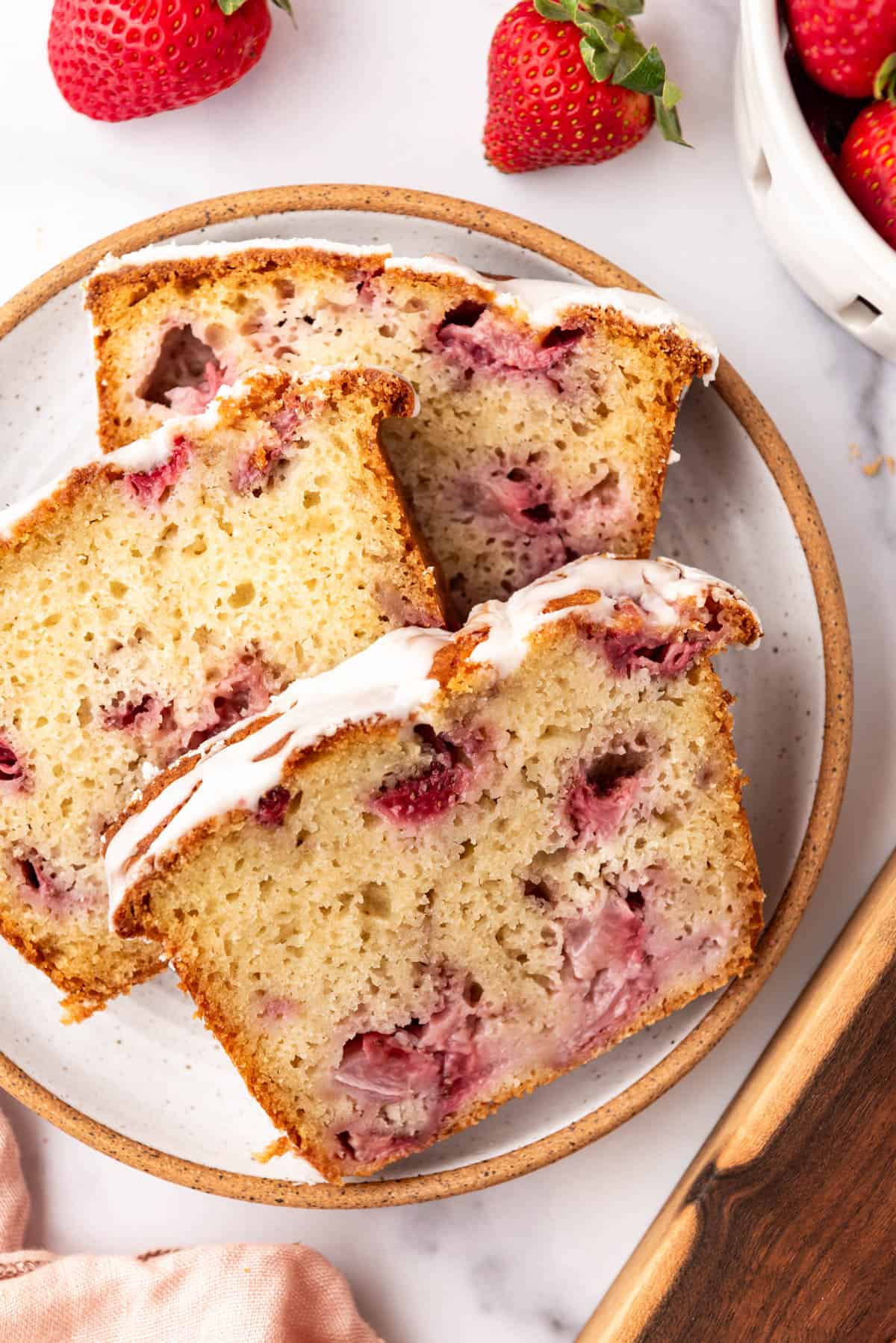 An overhead image of slices of moist strawberry quick bread on a plate surrounded by strawberries.