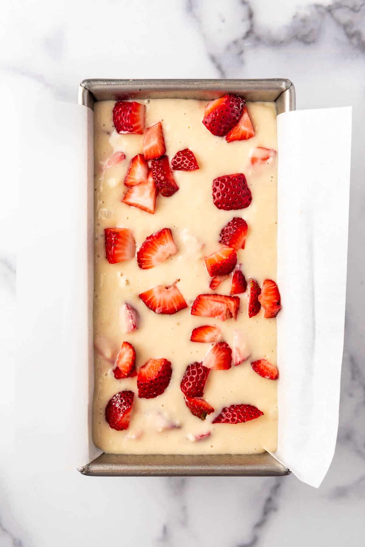 Strawberry bread batter in a loaf pan with chopped strawberries sprinkled on top.