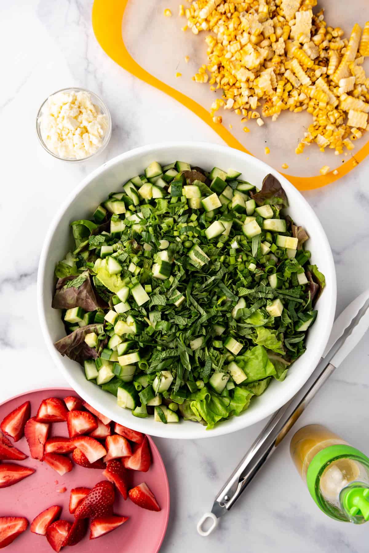 An overhead image of a large salad bowl filled with butter lettuce, diced cucumber, and chopped fresh basil and mint.