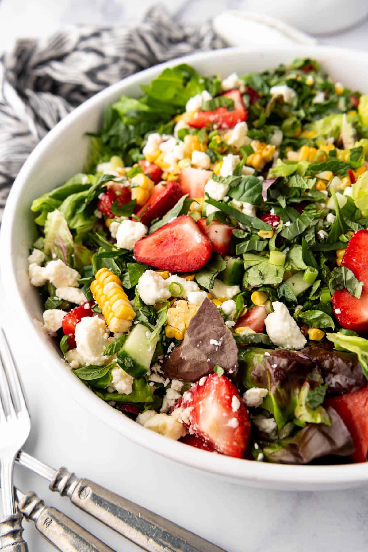 An image of a summer salt made with strawberries, corn, feta, and fresh herbs in a large white salad bowl. 