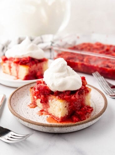 Slices of strawberry shortcake with whipped cream on plates in front of bowls of mashed strawberries and whipped cream.