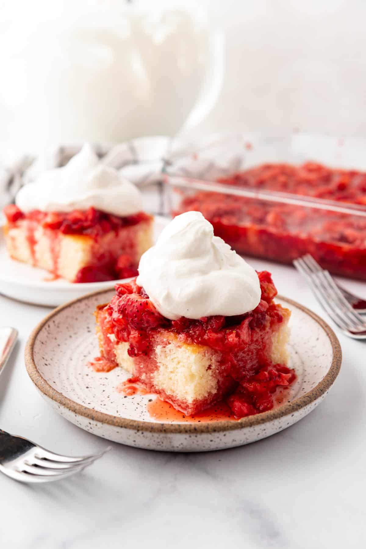 Slices of strawberry shortcake with whipped cream on plates in front of bowls of mashed strawberries and whipped cream.