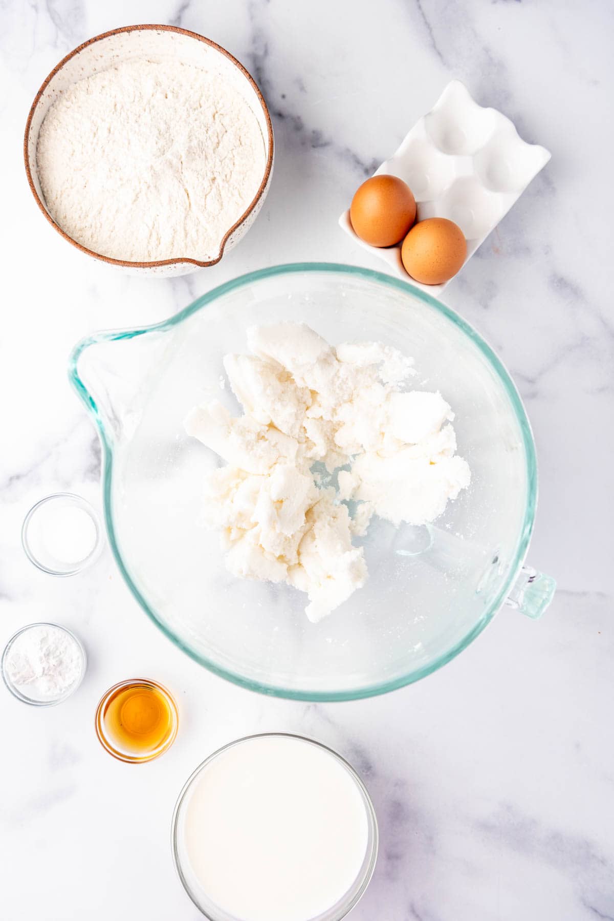 Creamed sugar and shortening in a glass mixing bowl with more ingredients surrounding the bowl.