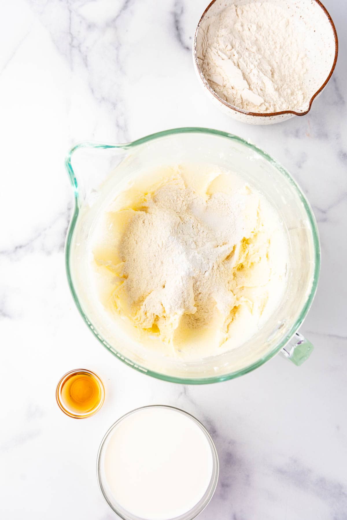 Adding dry ingredients to cake batter in a large glass mixing bowl.