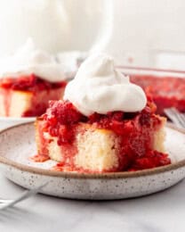 Slices of strawberry shortcake with whipped cream on plates in front of bowls of mashed strawberries and whipped cream.