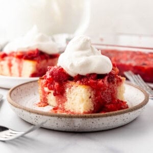 Slices of strawberry shortcake with whipped cream on plates in front of bowls of mashed strawberries and whipped cream.