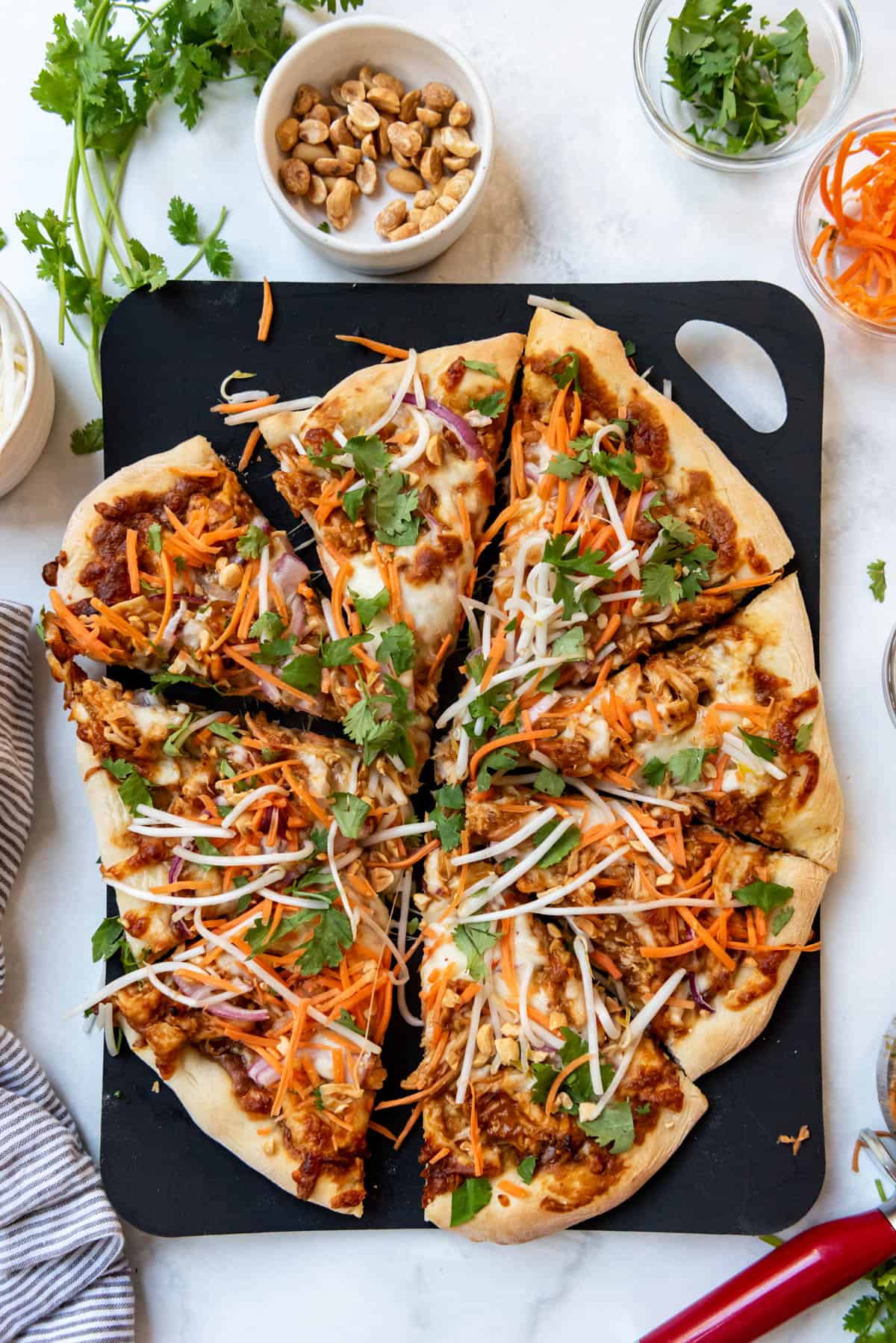 A sliced Thai chicken pizza on a black cutting board.